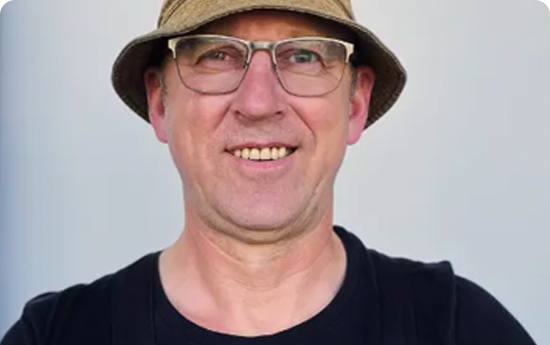 A man with glasses and a hat smiling warmly.