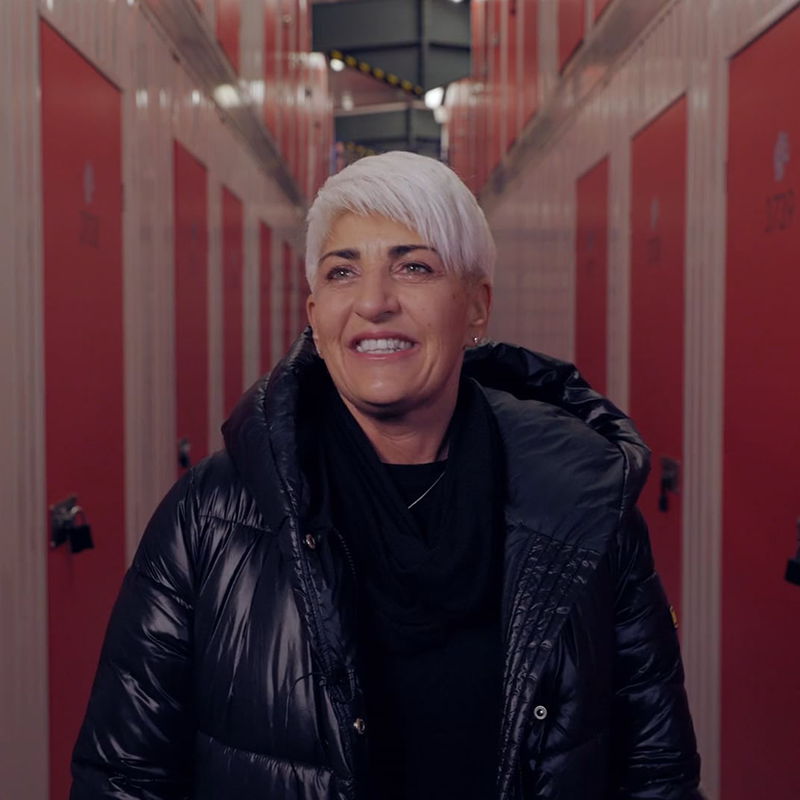 A woman with white hair and a black jacket stands in a hallway near the storage doors of Elephant Click & Store.