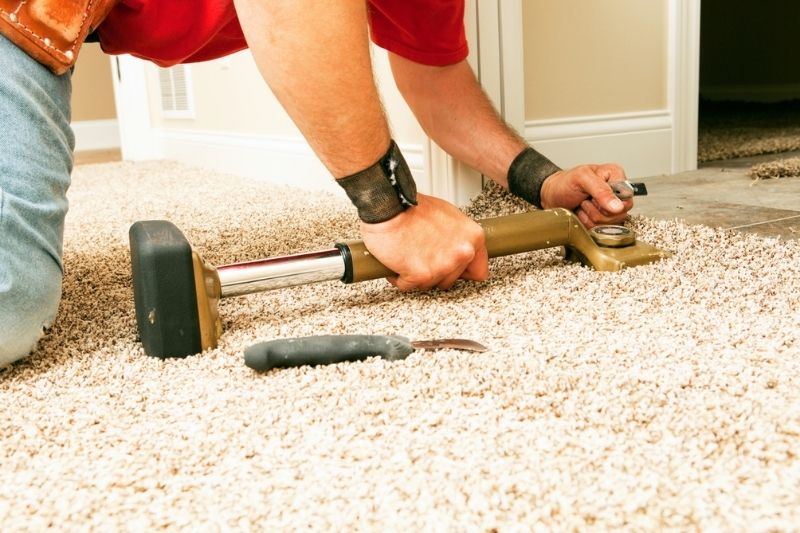 A man installing carpet using a tool.