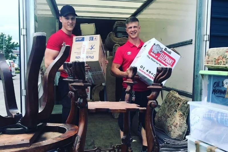 Two men in red shirts carrying boxes and furniture while moving into a new home.