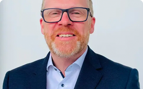 A man with glasses and a beard wearing a suit, looking professional and confident.