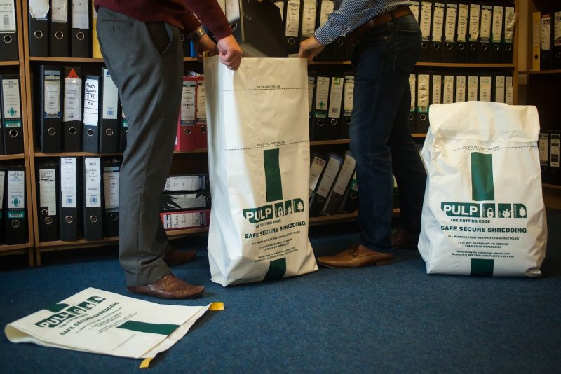 Two men holding bags of paper in a room, engaged in safe secure shredding.