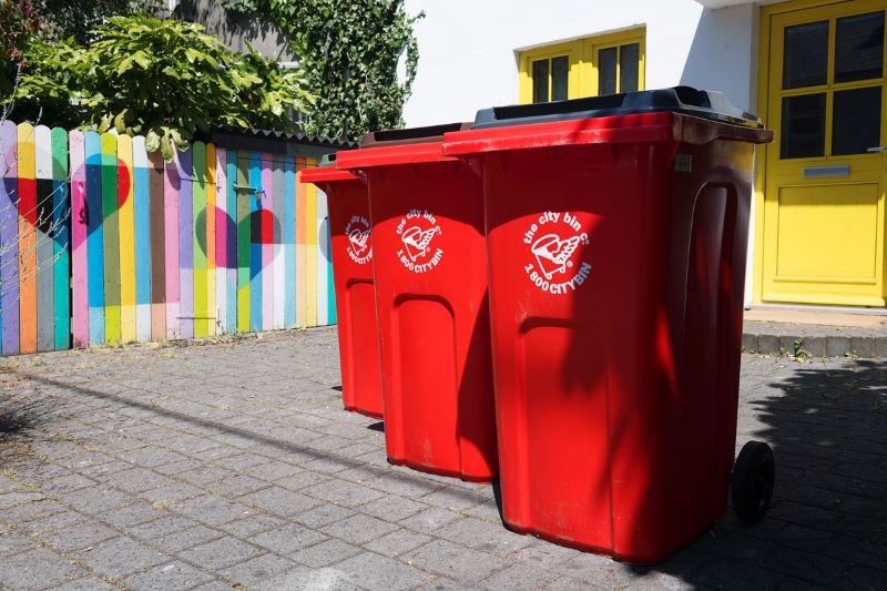 Three red trash cans lined up in front of a colorful wall.