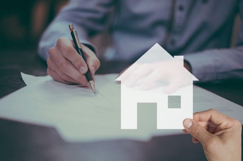 A man signing a contract with a house on paper, symbolizing a real estate agreement.