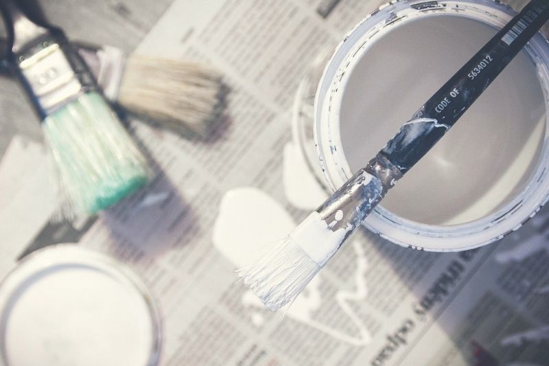 A paint brush and paint can on a newspaper, depicting an artistic scene with vibrant colors.