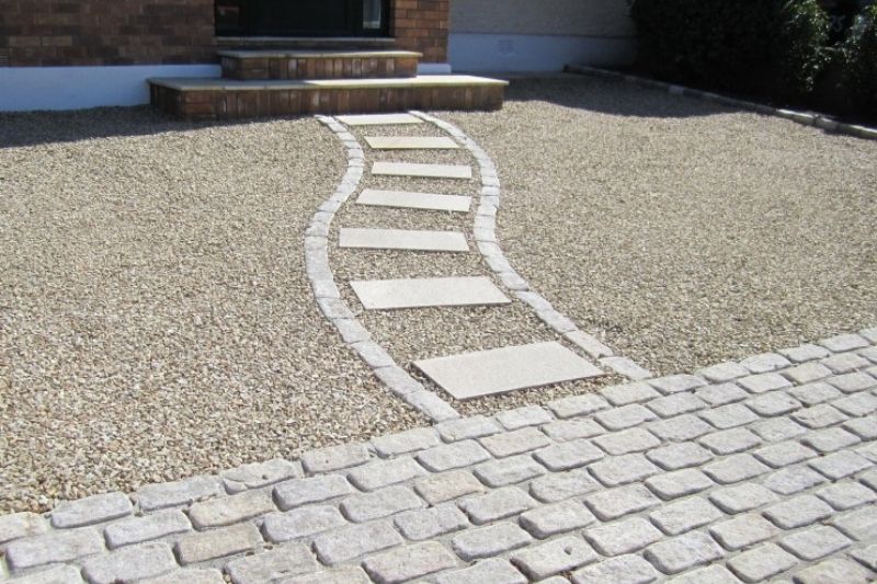 A gravel driveway with steps leading to a house, surrounded by greenery and a well-maintained landscape.